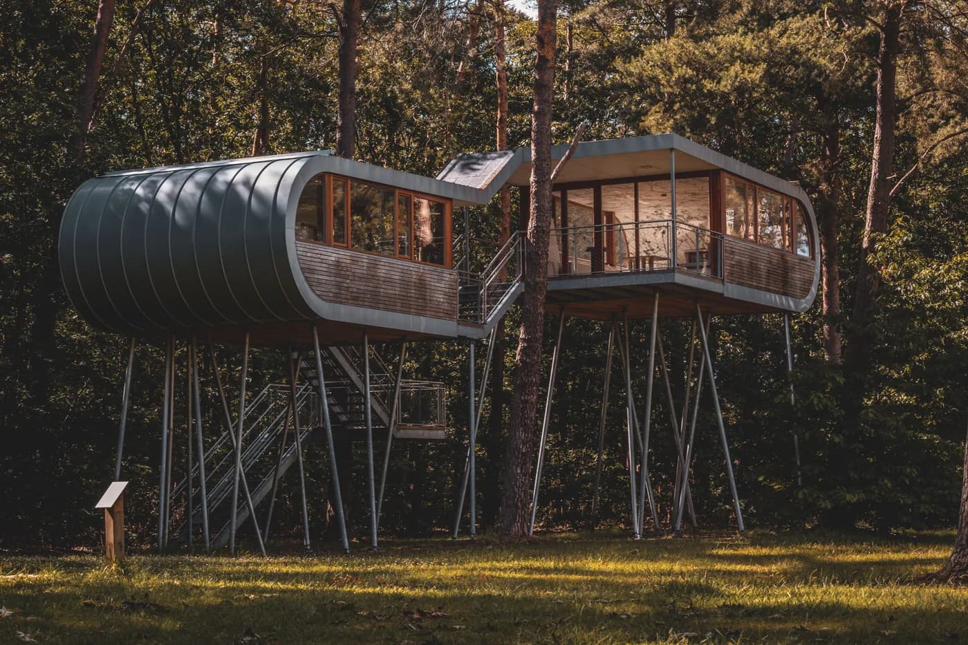 Exemple d'image BookNoFees : deux cabanes modernes sur pilotis, avec des escaliers métalliques entre les arbres de la forêt