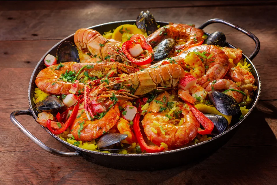 BookNoFees: Beispielfoto: Eine Pfanne mit Meeresfrüchte-Paella, garniert mit Schalentieren und roten Paprikaschoten