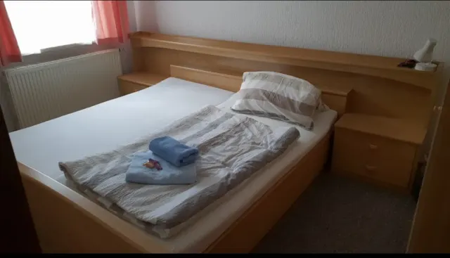 BookNoFees: casa vacanza a Schönfeld – Camera da letto con letto in legno, asciugamani piegati e finestra con tende rosa