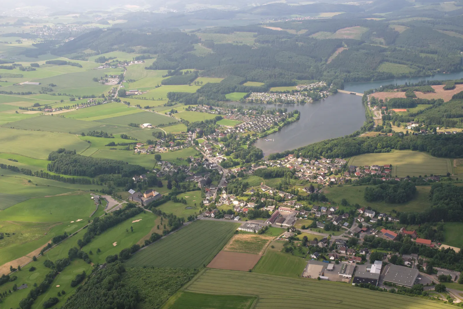 Der Sorpesee aus der Vogelperspektive, mit dem Dorf Amecke an seinem östlichen Ufer und den bewaldeten Hügeln des Sauerlands im Hintergrund