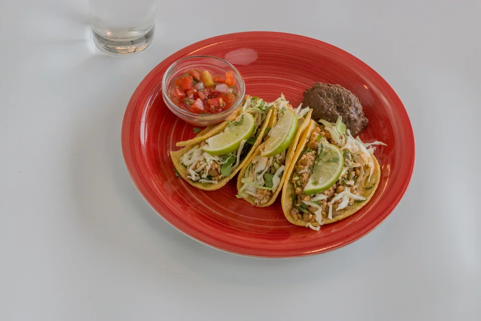 BookNoFees: Beispielfoto: Drei Tacos mit Limettenscheiben garniert, mit Salsa auf einem roten Teller