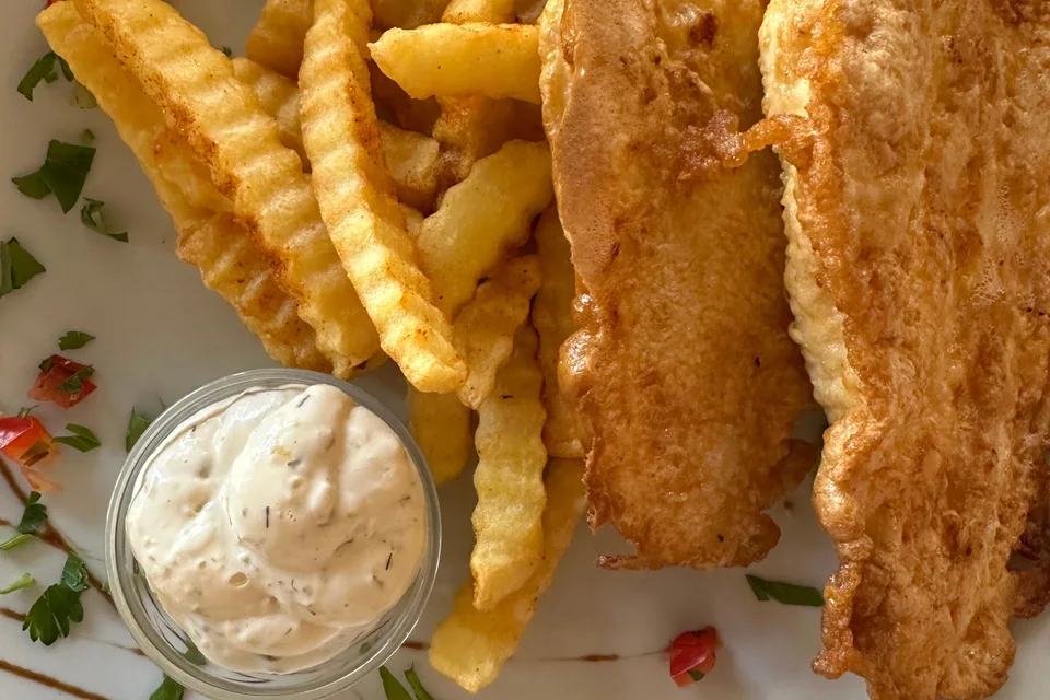 BookNoFees: Photo d’illustration : Filets de poisson panés accompagnés de frites ondulées et d'un petit bol de sauce
