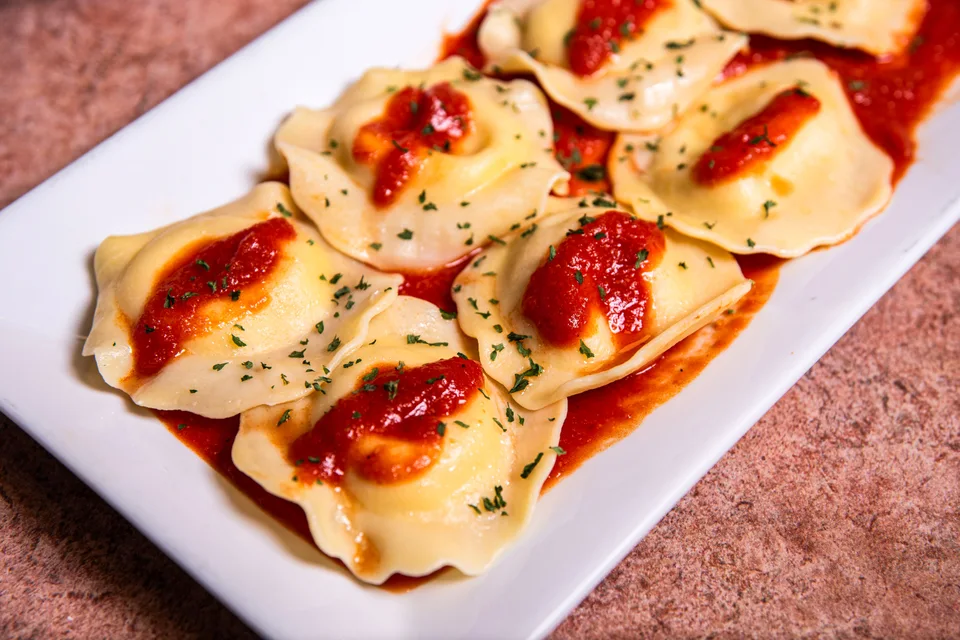 Foto di esempio: Ravioli conditi con salsa di pomodoro ed erbe aromatiche su un piatto bianco